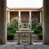 Jardín peristilo romano iluminado por el sol con columnata de mármol, setos cuidadosamente recortados y una fuente central, el tipo de jardín cerrado que las figuras guardianas grecorromanas protegían.