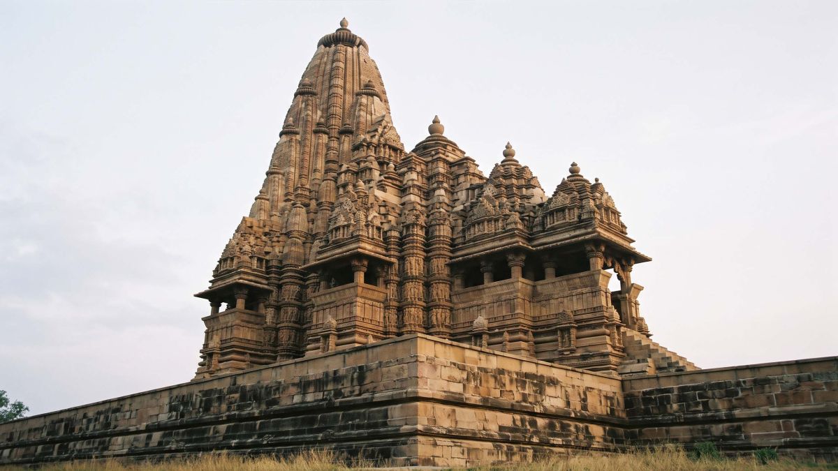 Un visitante de pie en la base de un templo de arenisca tallada de Khajuraho, en Madhya Pradesh, durante la hora dorada, empequeñecido por sus muros de relieves en bandas y su aguja escalonada.