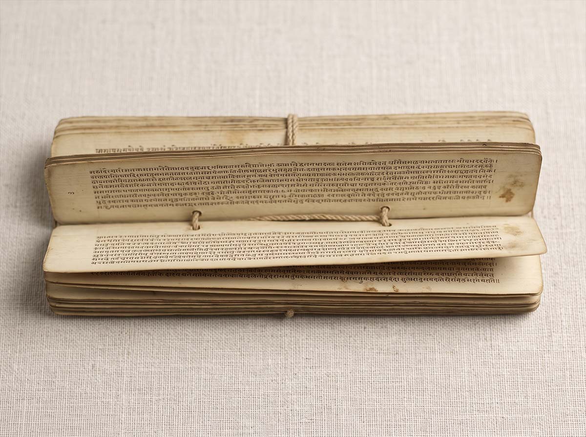 Detail of an open Sanskrit manuscript on a neutral surface under soft museum lighting