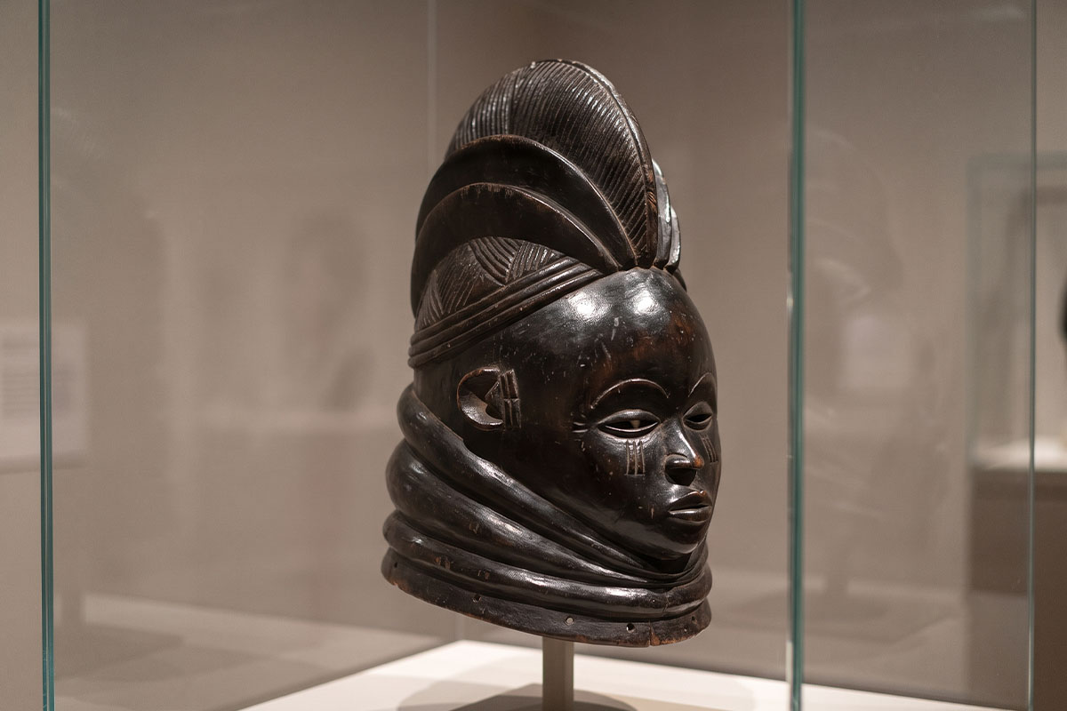 A carved wooden Sowei helmet mask of the Sande society displayed in a museum vitrine
