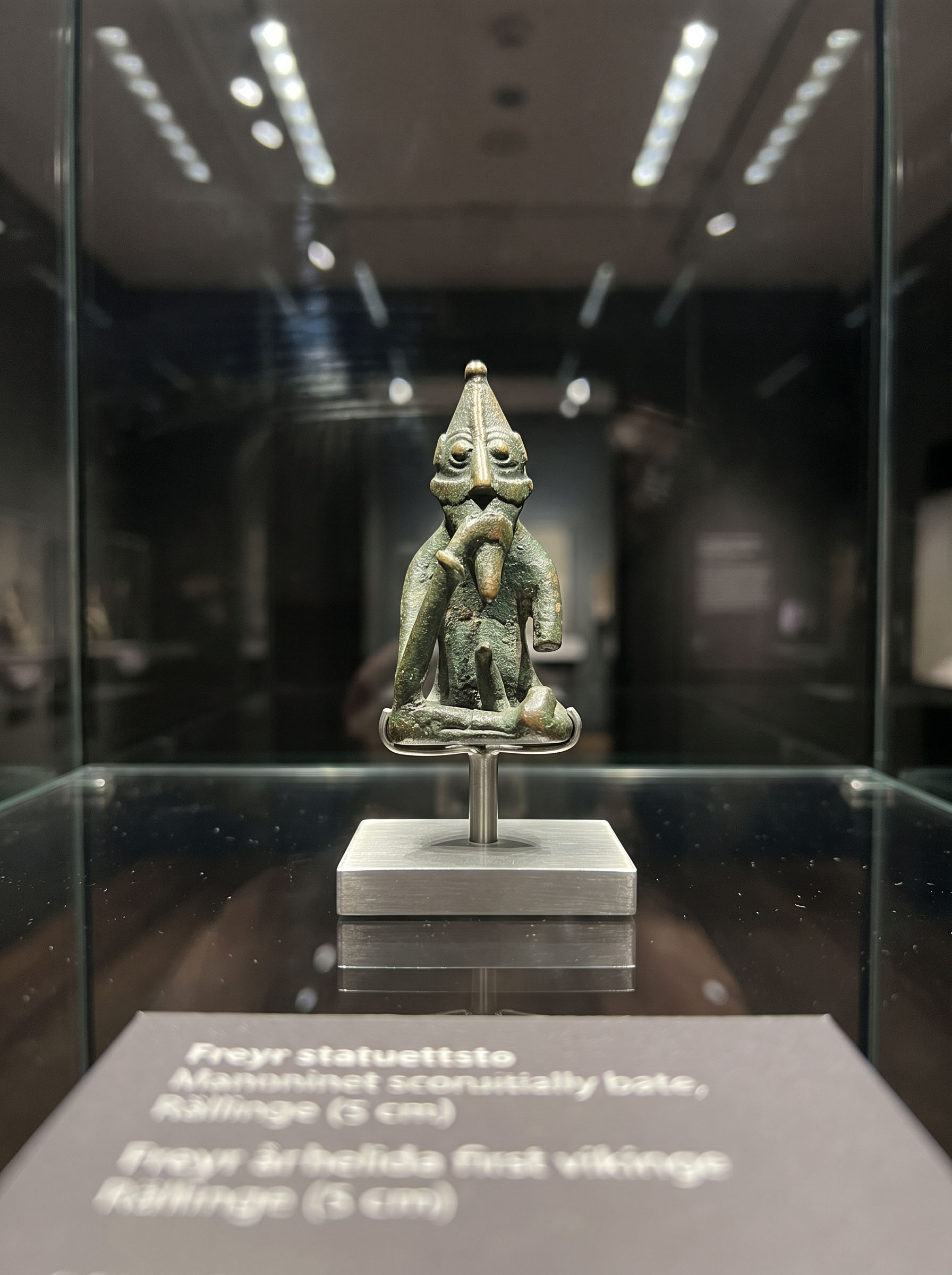 A small Viking Age bronze figurine displayed on a mount inside a lit museum vitrine