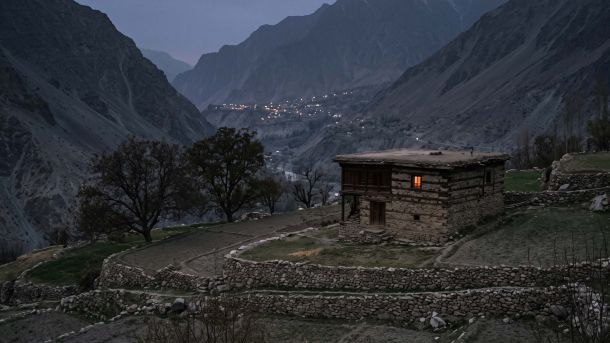 A lamplit stone seclusion house set apart below a terraced mountain village at dusk, illustrating menstruation taboos documented by anthropologists