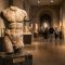 A weathered ancient stone sculpture representing historical ideals of masculinity and power.